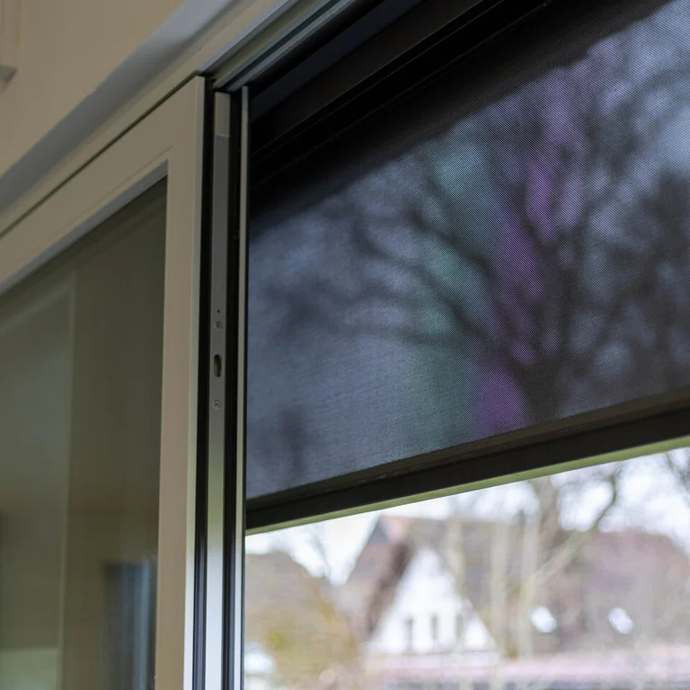Textilscreen mit dunklem Gewebe vor einem Fenster als außenliegender Sicht- und Sonnenschutz